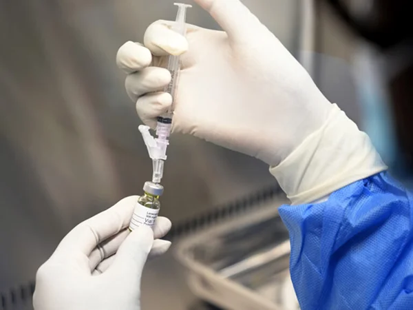 Technician handling an injectable vial with a syringe in a controlled laboratory environment.