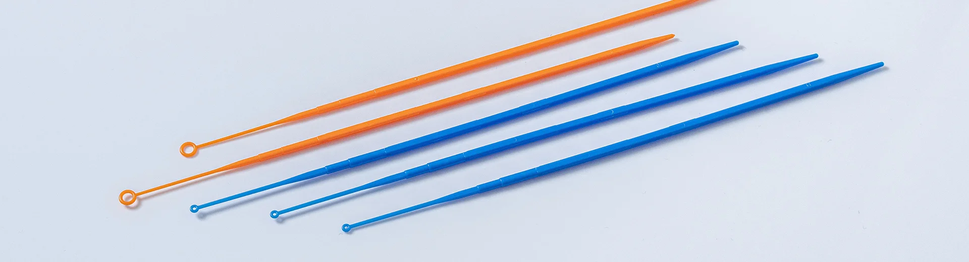 Blue and orange disposable inoculating loops and needles are arranged side by side.