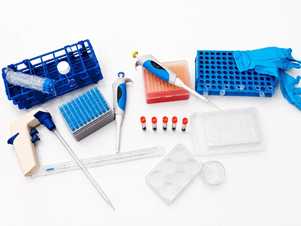 Laboratory pipettes, racks, gloves, tubes and multiwell plates arranged on a white surface.