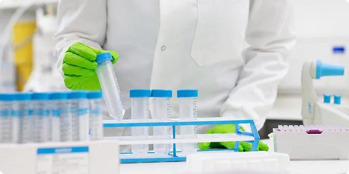 A laboratory researcher transfers liquid into a centrifuge tube at a clean lab bench.