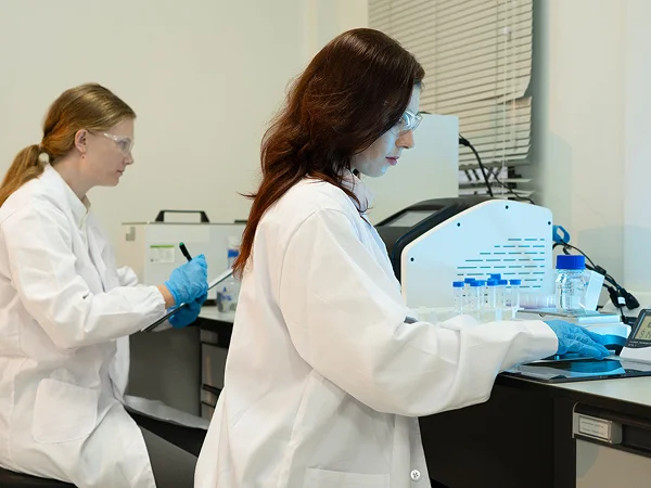 Two laboratory researchers operating analytical instruments and viewing data on computer monitors.
