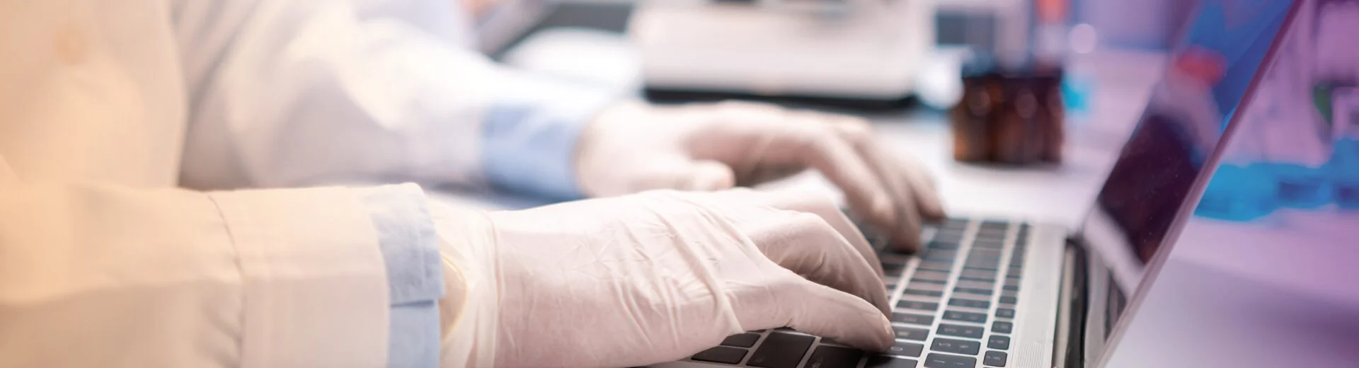 A gloved laboratory professional working on a computer in the laboratory.