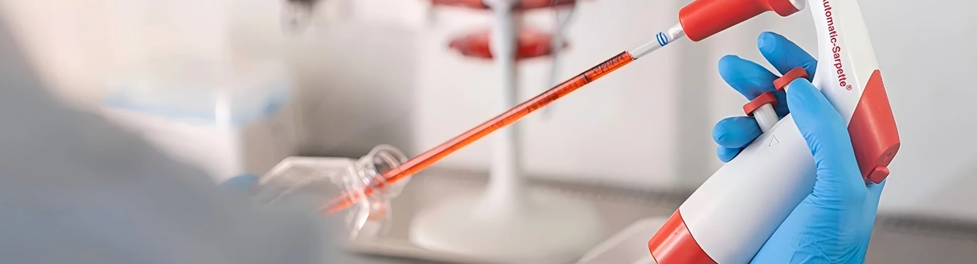 A gloved technician transfers liquid using a pipette controller and serological pipette.