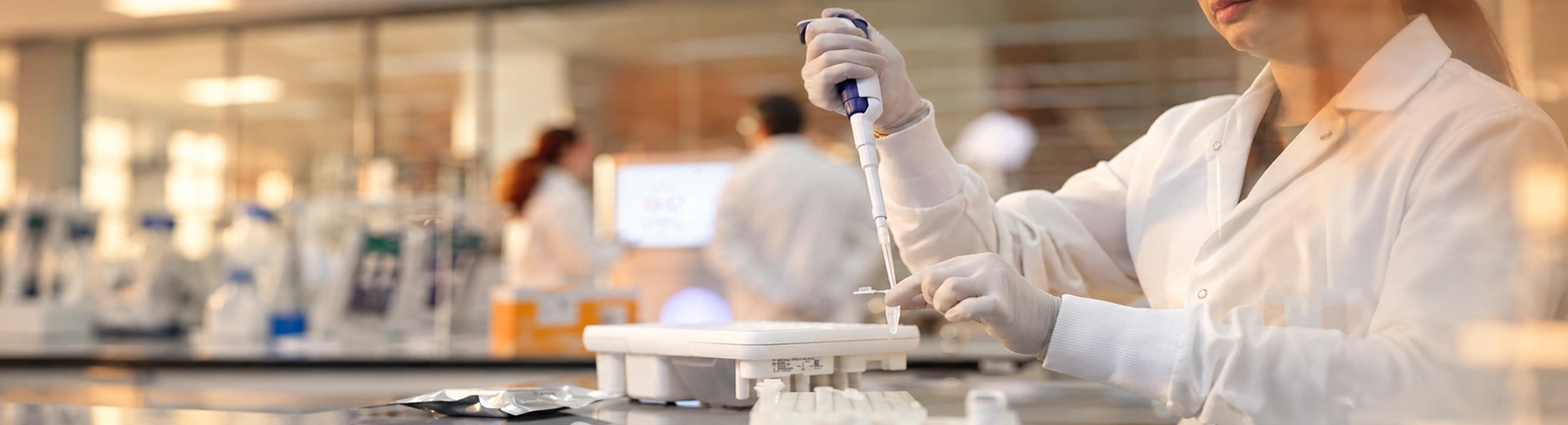 A laboratory worker wearing safety glasses and gloves pipettes liquid into a PCR tube.
