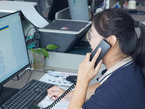 A staff member talks on the phone and takes notes at a computer.