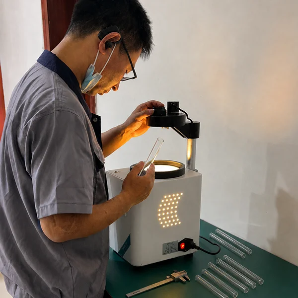 A technician inspects a clear glass test tube using an illuminated glass stress testing instrument.