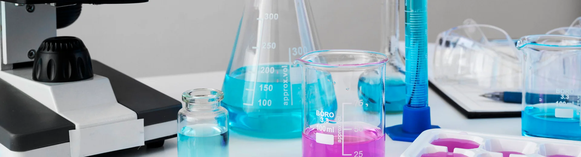 Beakers, cylinders, and cell culture consumables arranged beside a microscope.