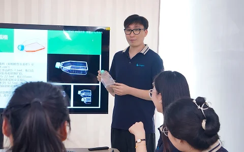 A sales manager presents lab supplies to colleagues, holding a cell culture flask.